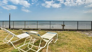 Two white lounge chairs with blue cushions on a grassy area near a black metal fence overlooking a body of water. - Daytona Beach Vacation Rental w/ Pool Access (Daytona Beach Shores)