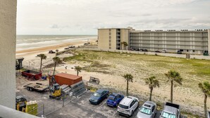 A parking area with several cars, a building with multiple floors, and a beach in the background. - Ocean Jewels Resort Studio w/ Community Perks! (Daytona Beach)