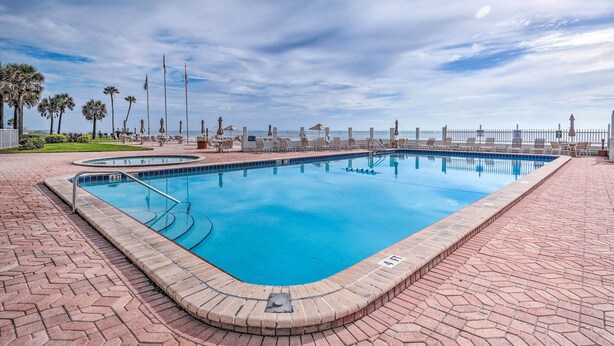 A rectangular swimming pool with a brick border, surrounded by a paved walkway. - Ocean Jewels Resort Studio w/ Community Perks! (Daytona Beach)