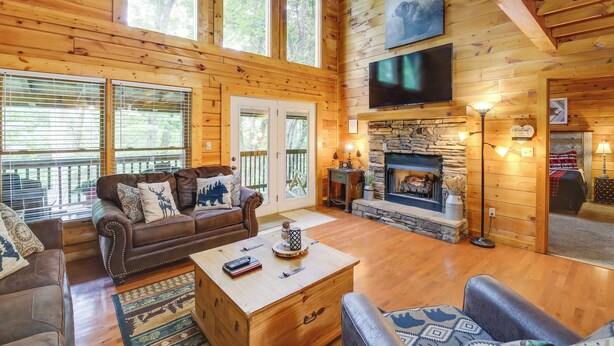 A log cabin interior with a fireplace, wooden walls, a sofa, and a television. - Hot Tub + Pool Table: Secluded Seiverville Cabin (Sevierville)