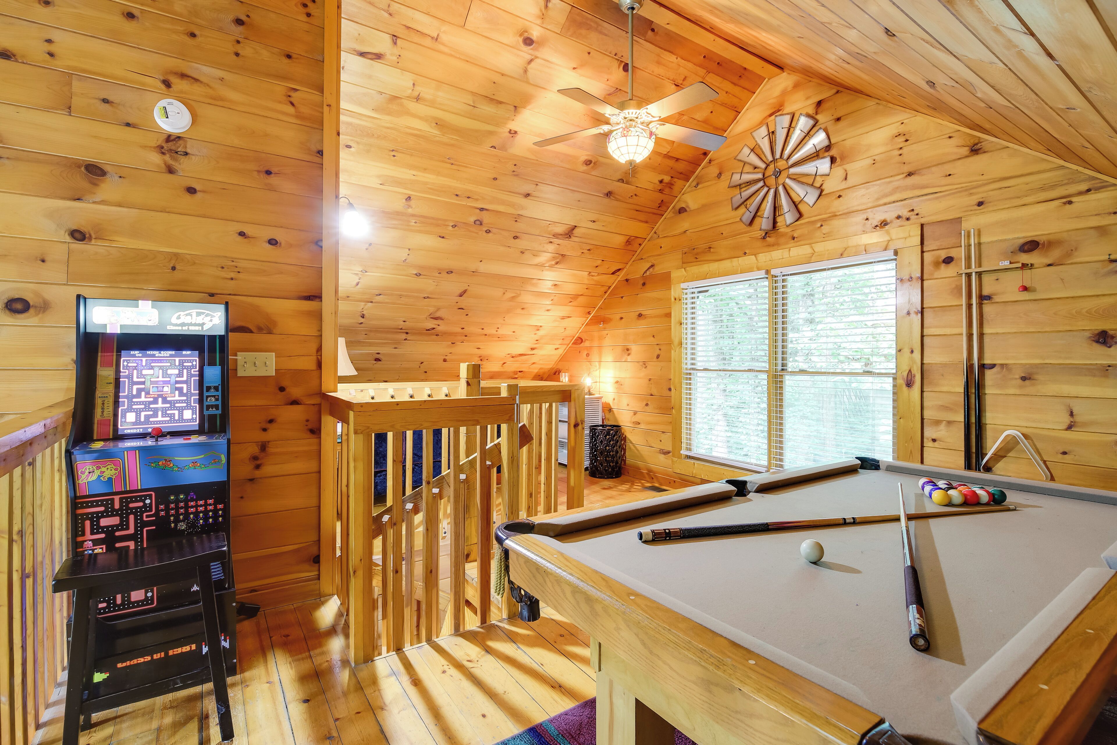 A wooden cabin with a pool table, a pinball machine, and a ceiling fan.