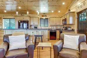 A cabin interior with a kitchen, dining area, and two leather chairs with cushions. - Gorgeous Gatlinburg Cabin: Large Deck & Hot Tub! (Gatlinburg)