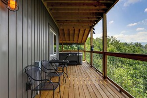 A wooden deck with a grill and chairs, overlooking a forested area. - Gorgeous Gatlinburg Cabin: Large Deck & Hot Tub! (Gatlinburg)