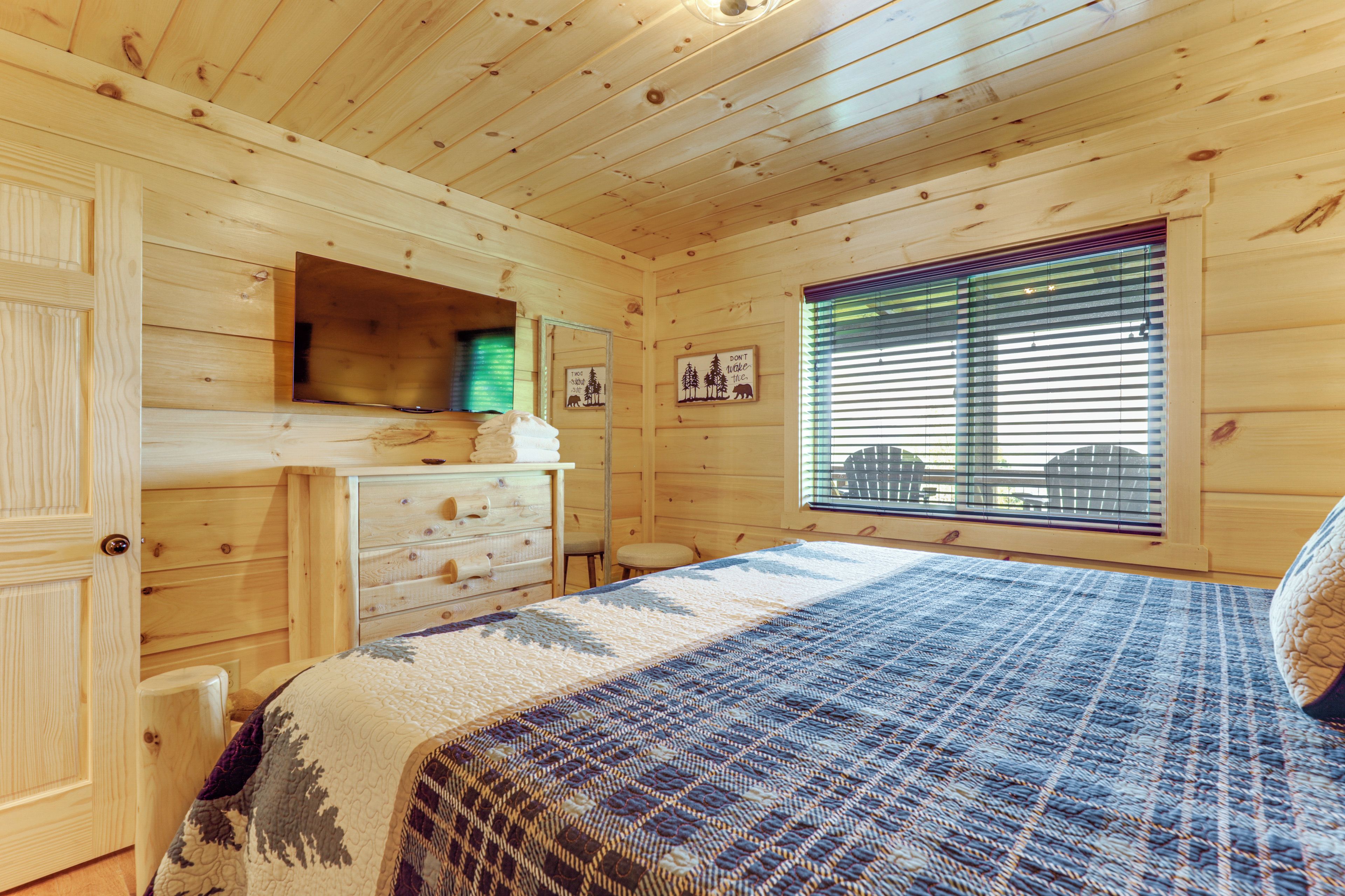 Une chambre dans une cabane en bois, avec un lit, une commode et une fenêtre équipée de stores.