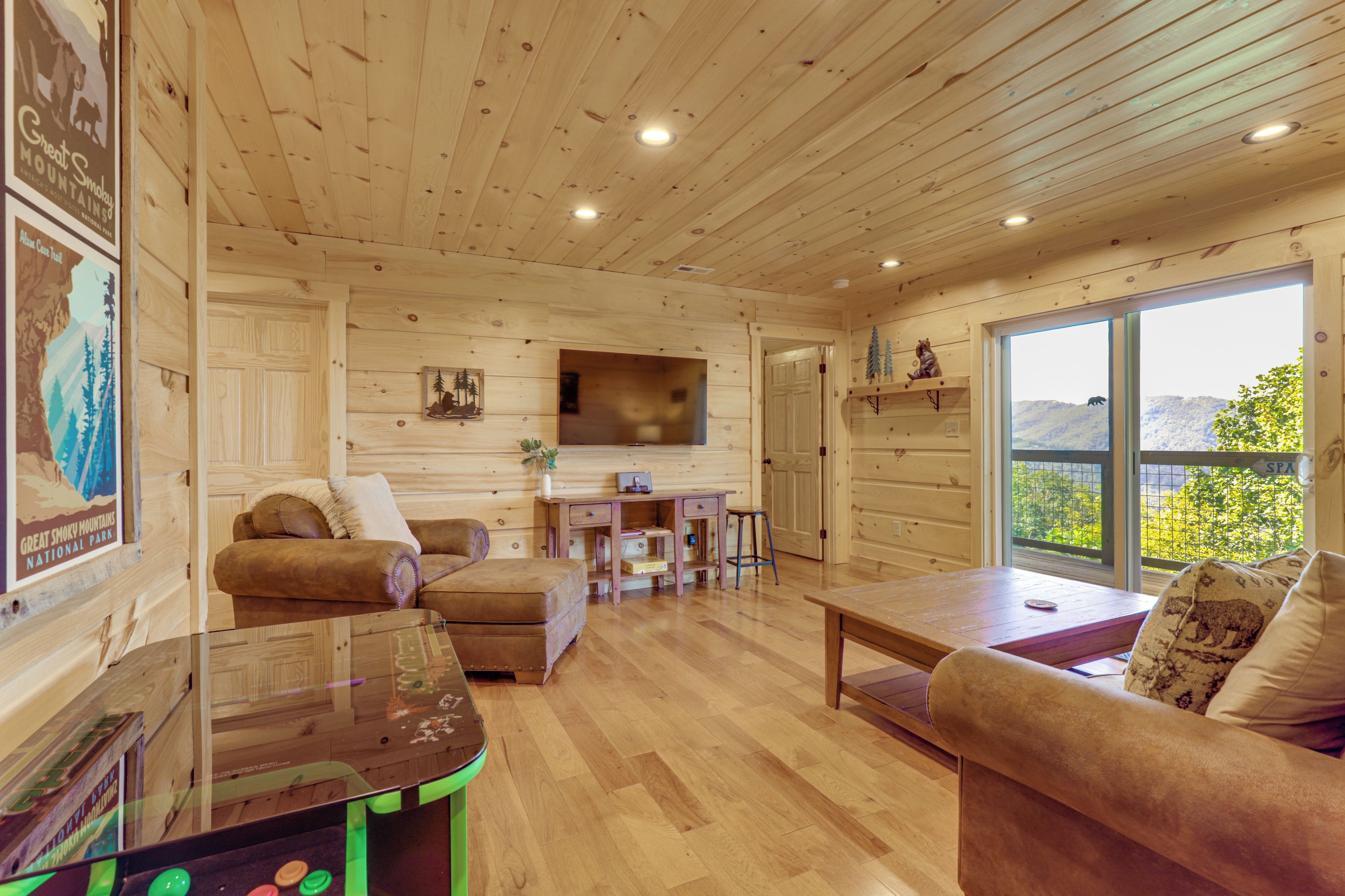Un acogedor interior de cabaña con paredes de madera, un sofá, una mesa de centro y un televisor montado en la pared.