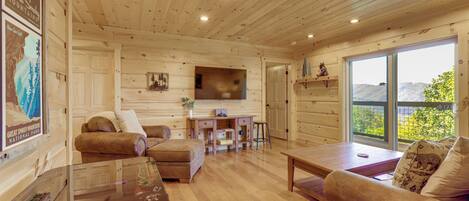 Un acogedor interior de cabaña con paredes de madera, un sofá, una mesa de centro y un televisor montado en la pared.