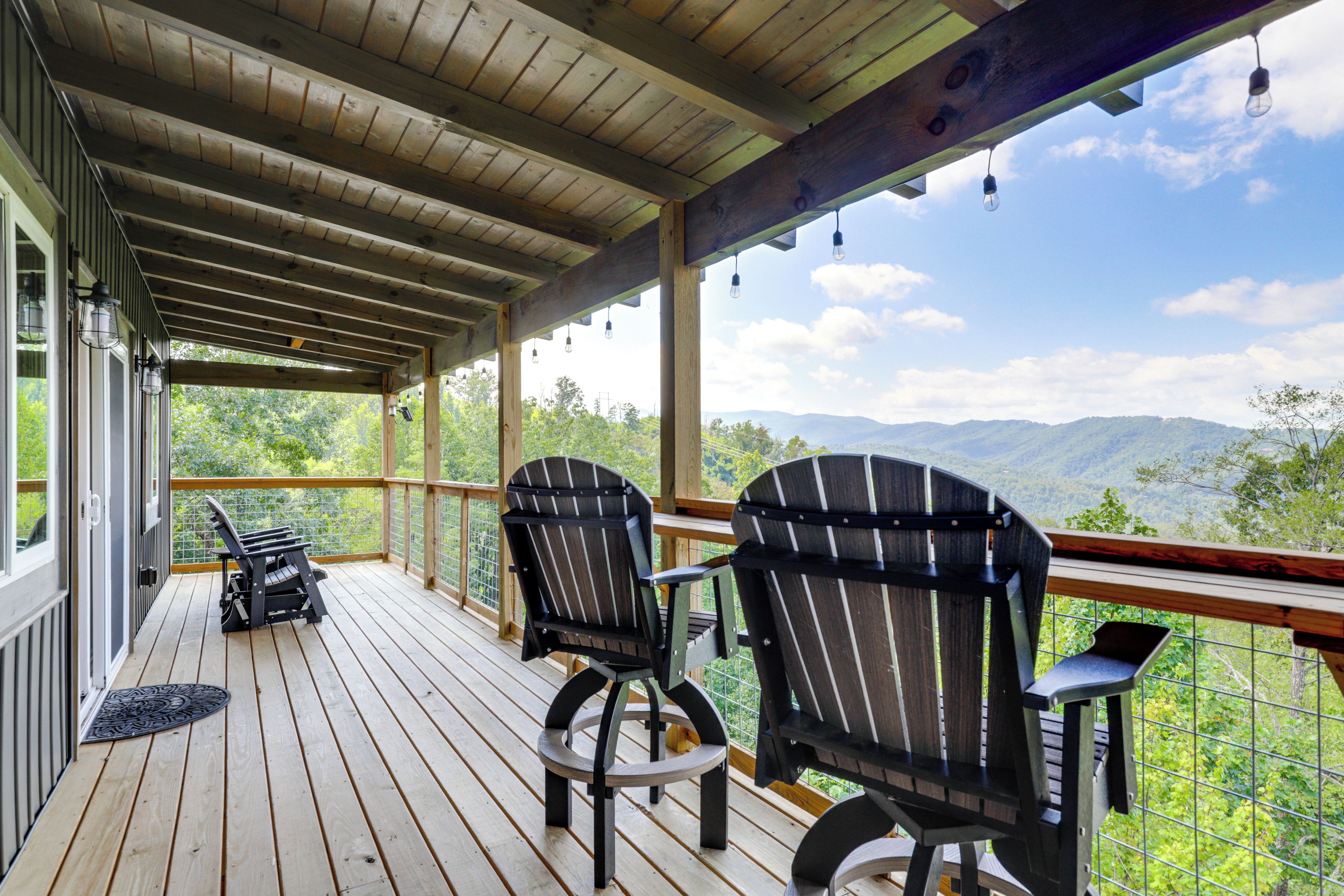 A wooden deck with Adirondack chairs and a view of mountains.