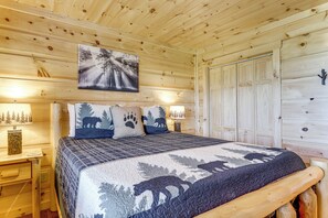 Une chambre à coucher dans une cabane en bois, avec un lit, un tableau représentant une forêt et une table de chevet avec une lampe.