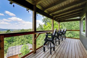 A wooden deck with outdoor seating and a view of a forested landscape. - Gorgeous Gatlinburg Cabin: Large Deck & Hot Tub! (Gatlinburg)