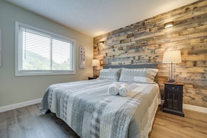 Quarto com cama grande, painéis de madeira, duas luminárias de cabeceira e janela com persianas.