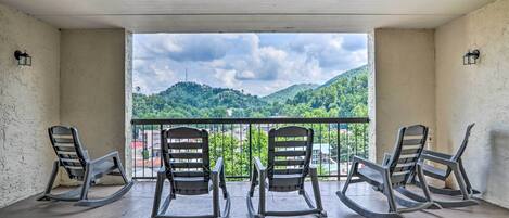 A balcony with three rocking chairs facing a scenic view of green hills and a cloudy sky.