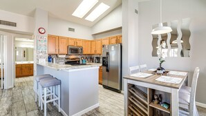 A modern kitchen with wooden cabinets, a central island, stainless steel appliances, and a dining area with a wooden table and chairs. - Walk to Rotary Park: Lake Havasu City Condo (Lake Havasu City)