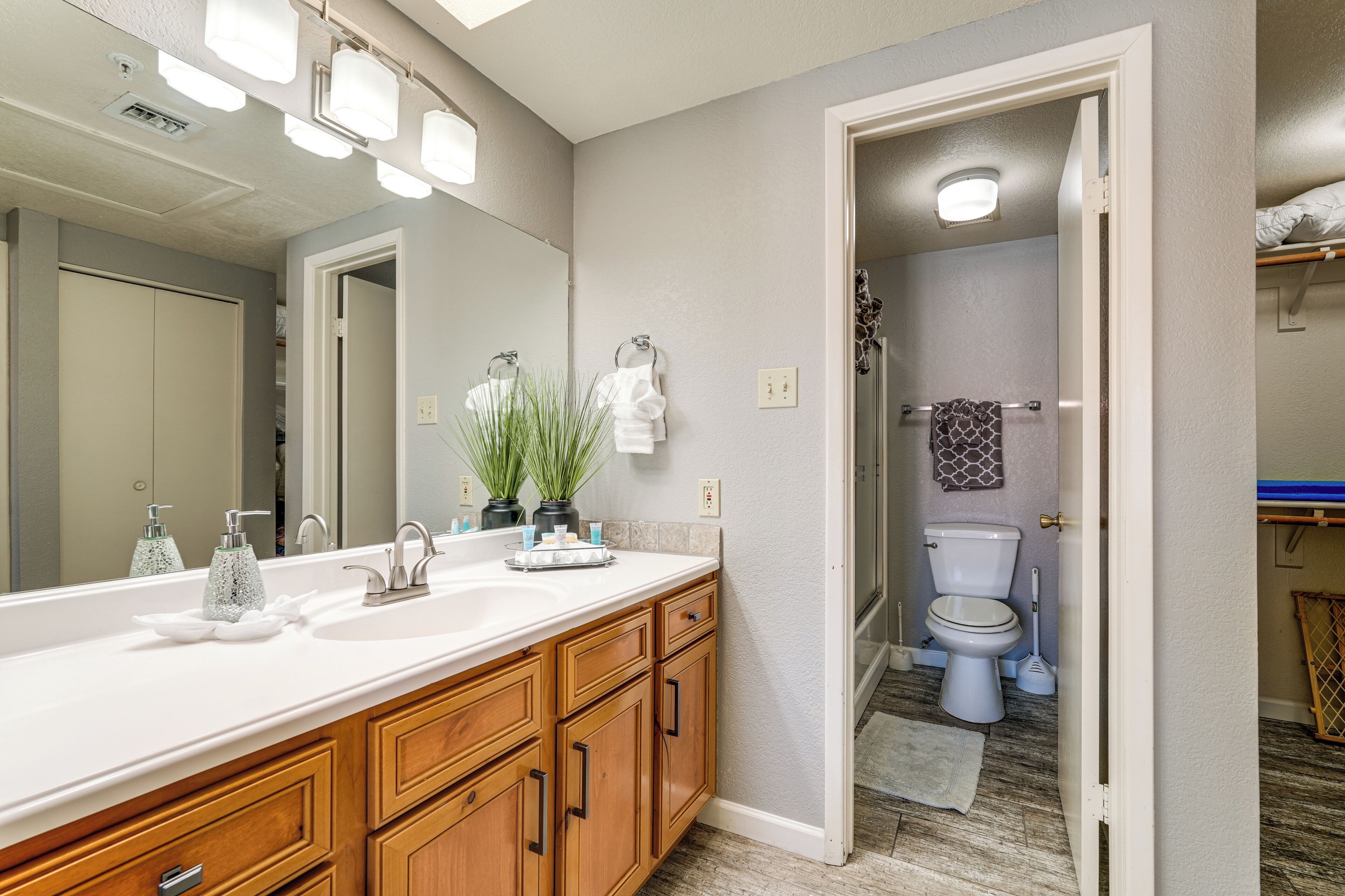 A bathroom with a large mirror, wooden vanity, and a toilet visible through an open door.