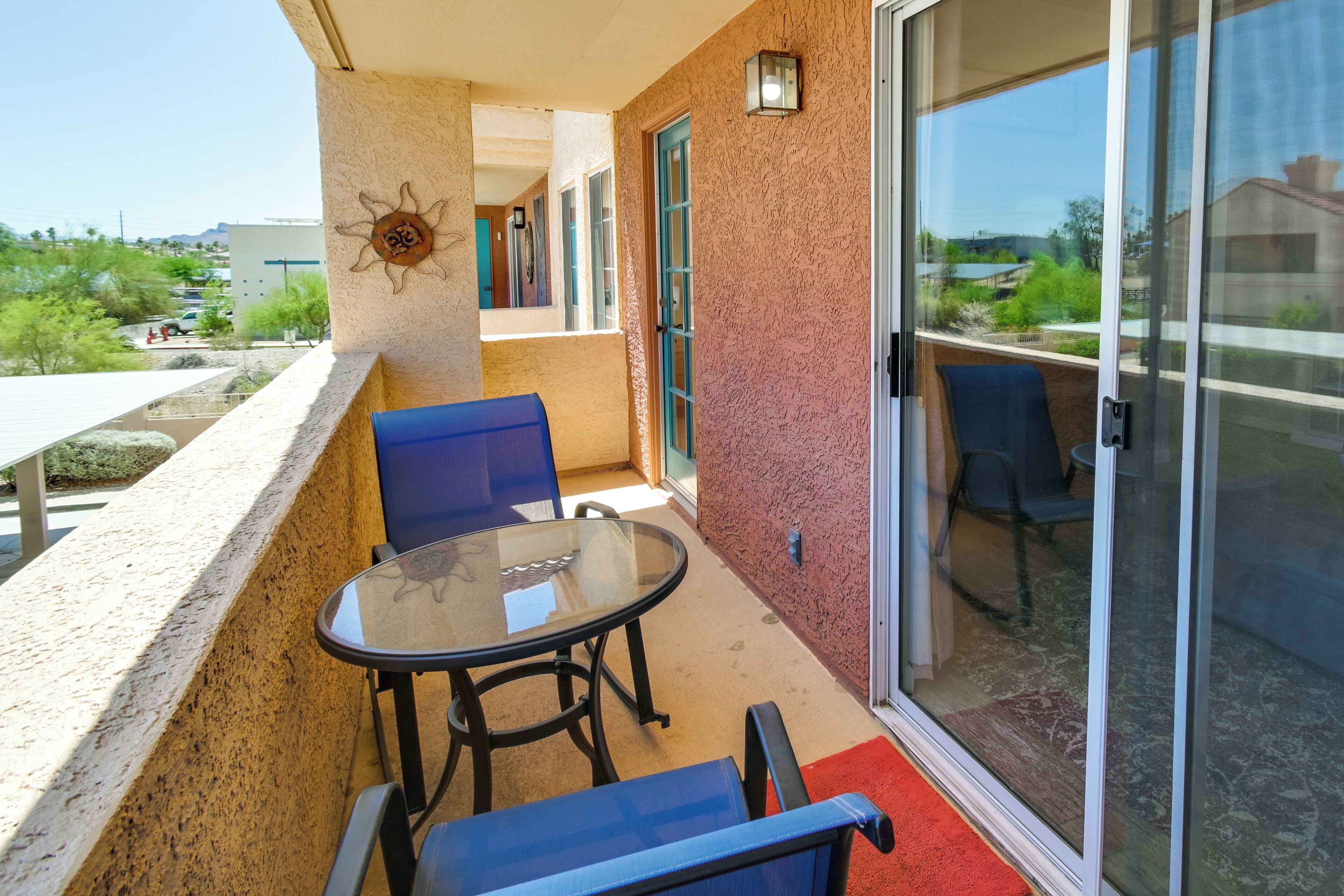 A balcony with a glass table and chairs, a red carpet, and a sliding glass door.