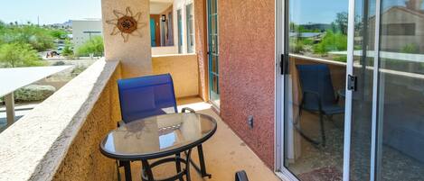 A balcony with a glass table and chairs, a red carpet, and a sliding glass door.
