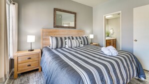 A neatly made bed with striped bedding, two bedside tables with lamps, a wooden headboard, and a mirror on the wall. - Walk to Rotary Park: Lake Havasu City Condo (Lake Havasu City)