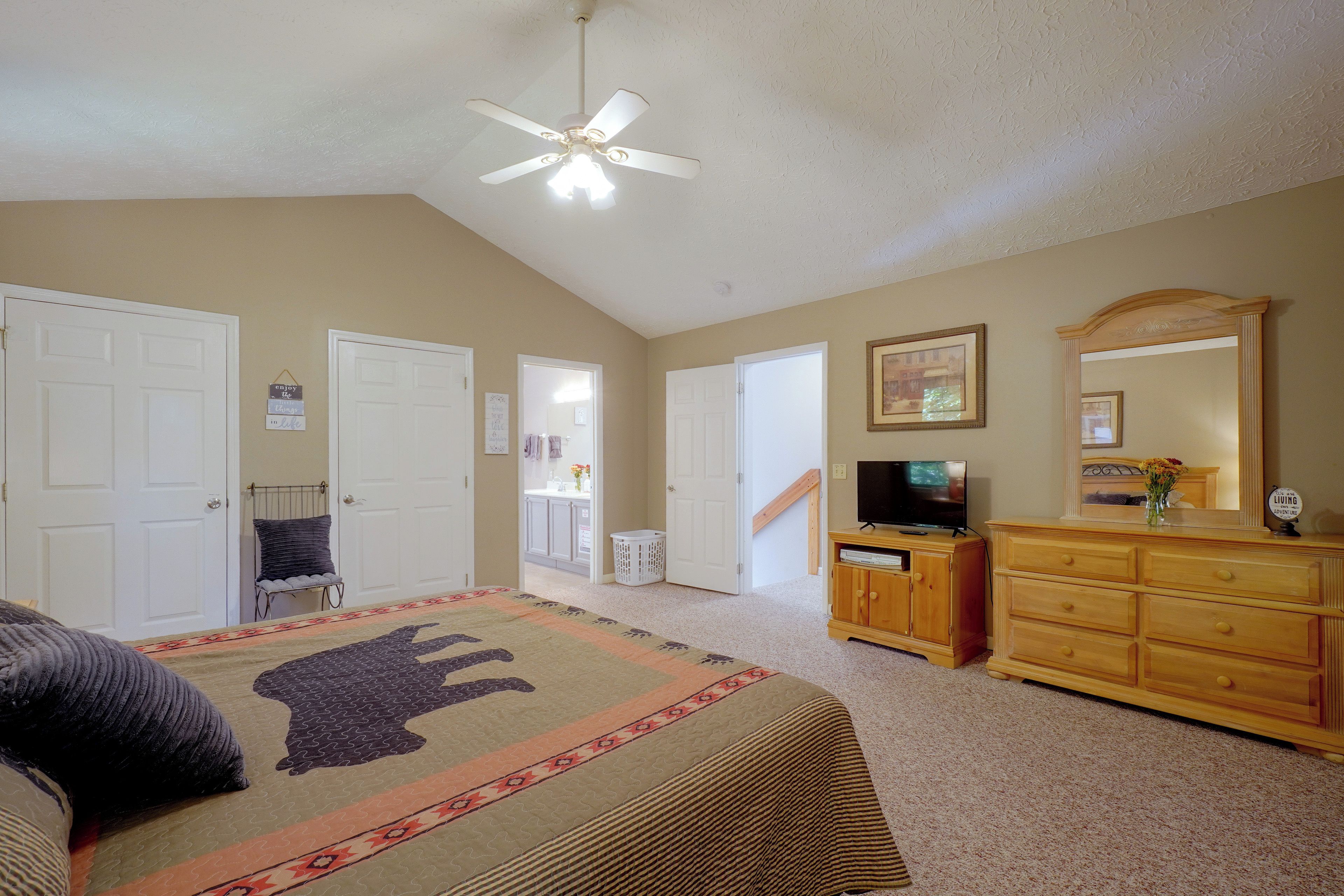 A bedroom with a bed, a dresser, a television, and a ceiling fan.