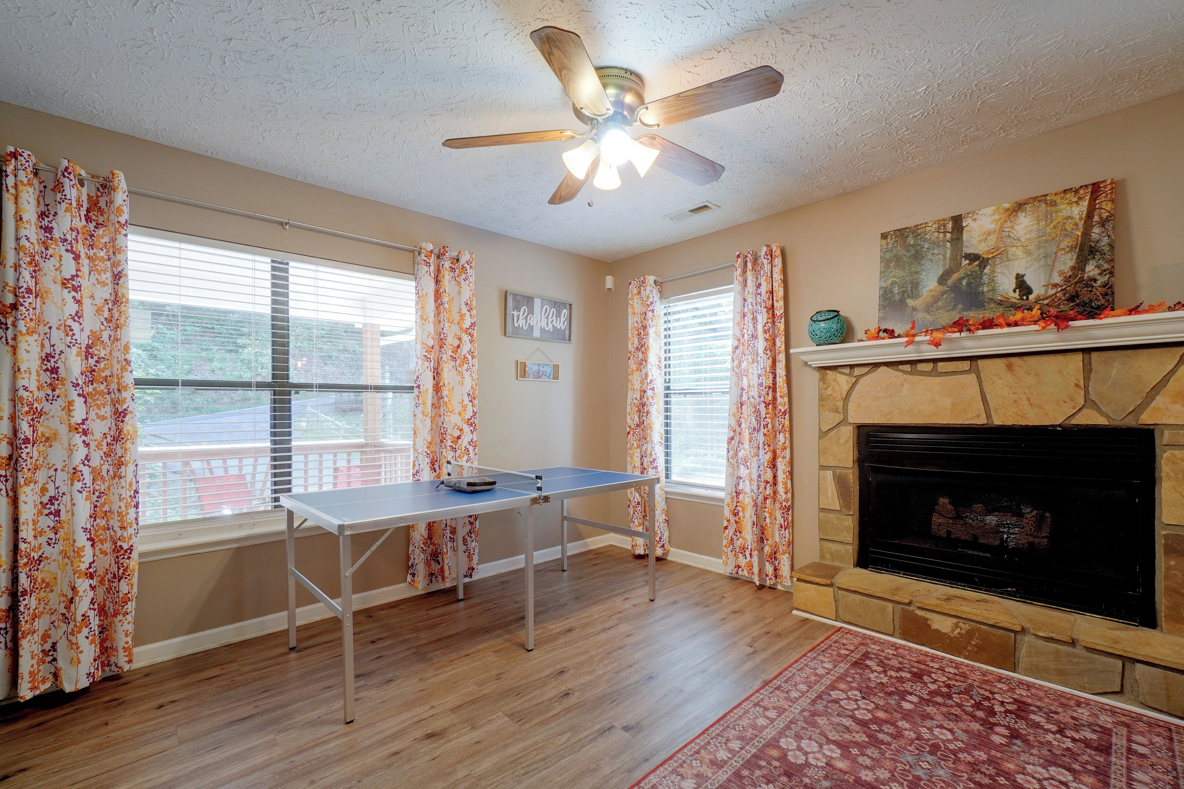 A room with a fireplace, a ceiling fan, and a ping pong table.