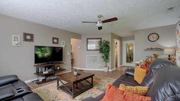 A living room with a television, leather sofas, a coffee table, and a ceiling fan.