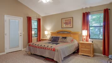A bedroom with a bed, two bedside tables, a nightstand, a ceiling fan, a door, and windows with curtains.