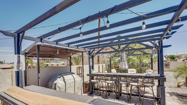 An outdoor patio with a grill, a table with chairs, and a pergola with hanging lights.