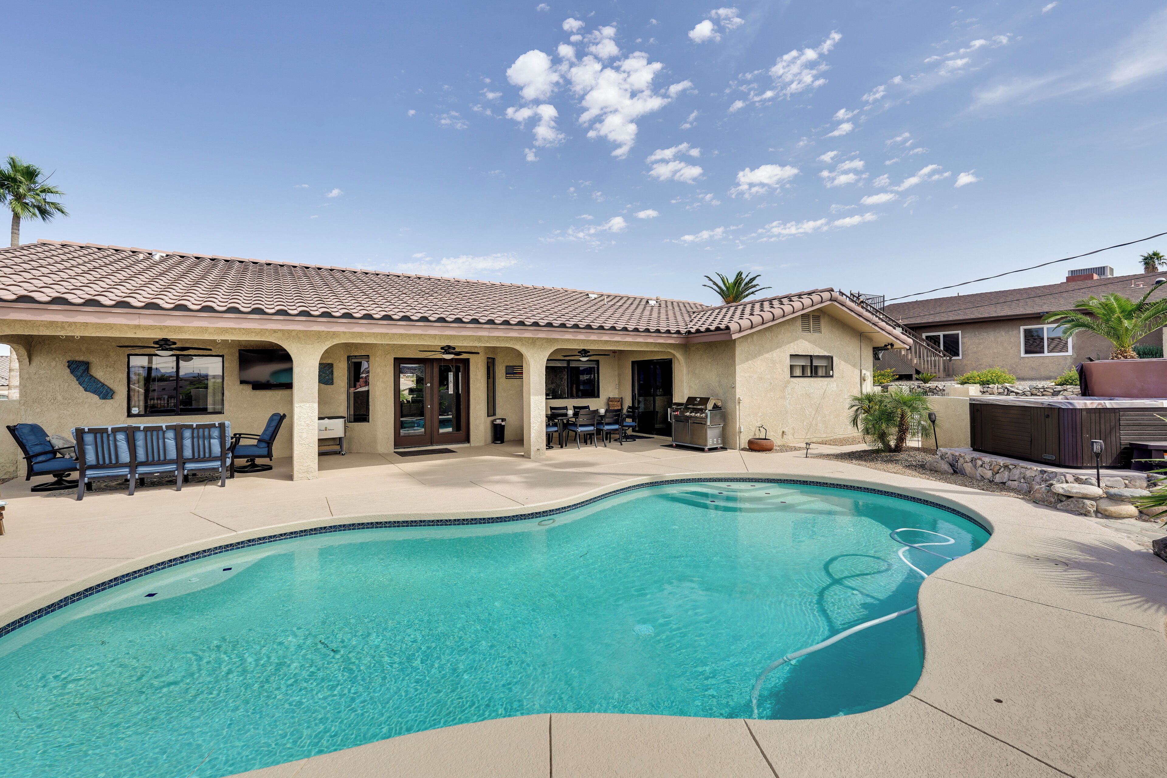 A backyard with a swimming pool, patio furniture, and a covered outdoor seating area.