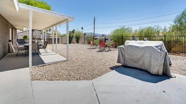 A covered patio area with outdoor seating, a barbecue grill, and a view of a desert landscape.