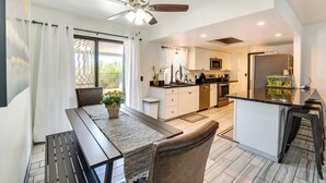 A modern kitchen with a central island, a dining area with a table and chairs, and a ceiling fan.
