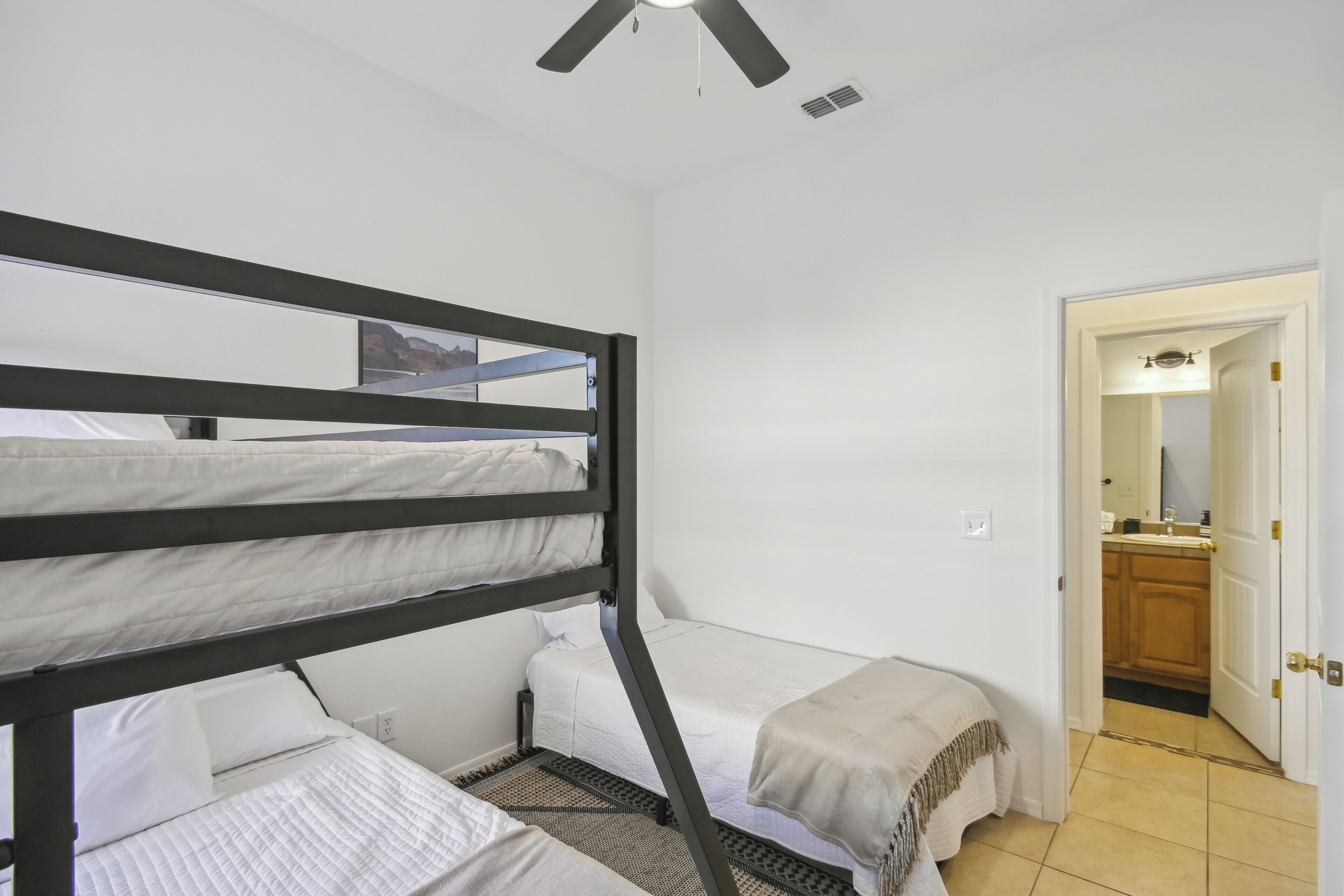 A room with bunk beds, a small desk, and a bathroom visible through an open door.