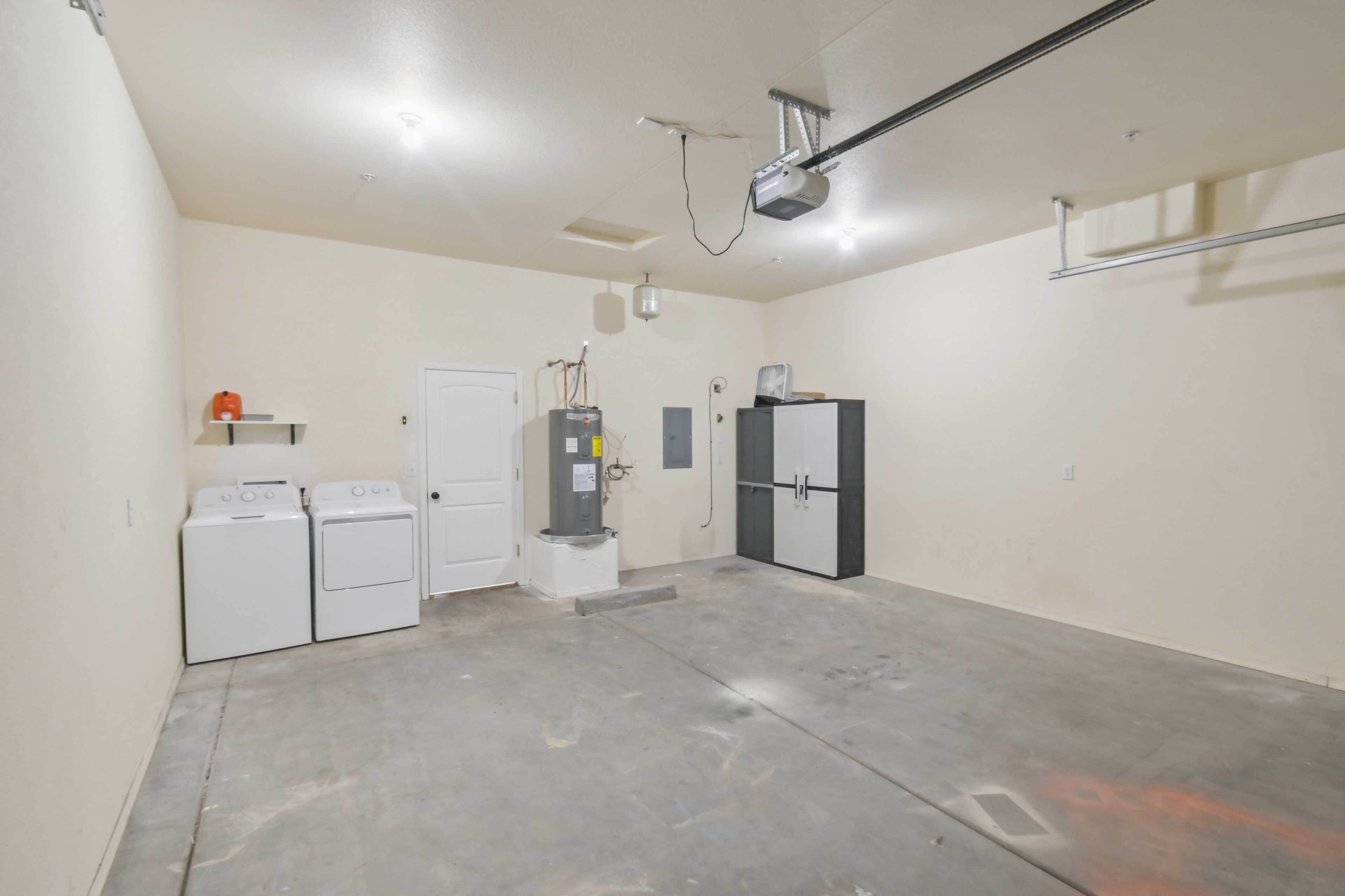 A laundry room with two washing machines, a dryer, a water heater, and a refrigerator.