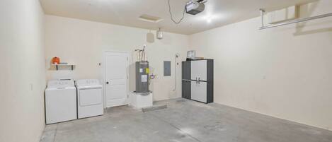 A laundry room with two washing machines, a dryer, a water heater, and a refrigerator.