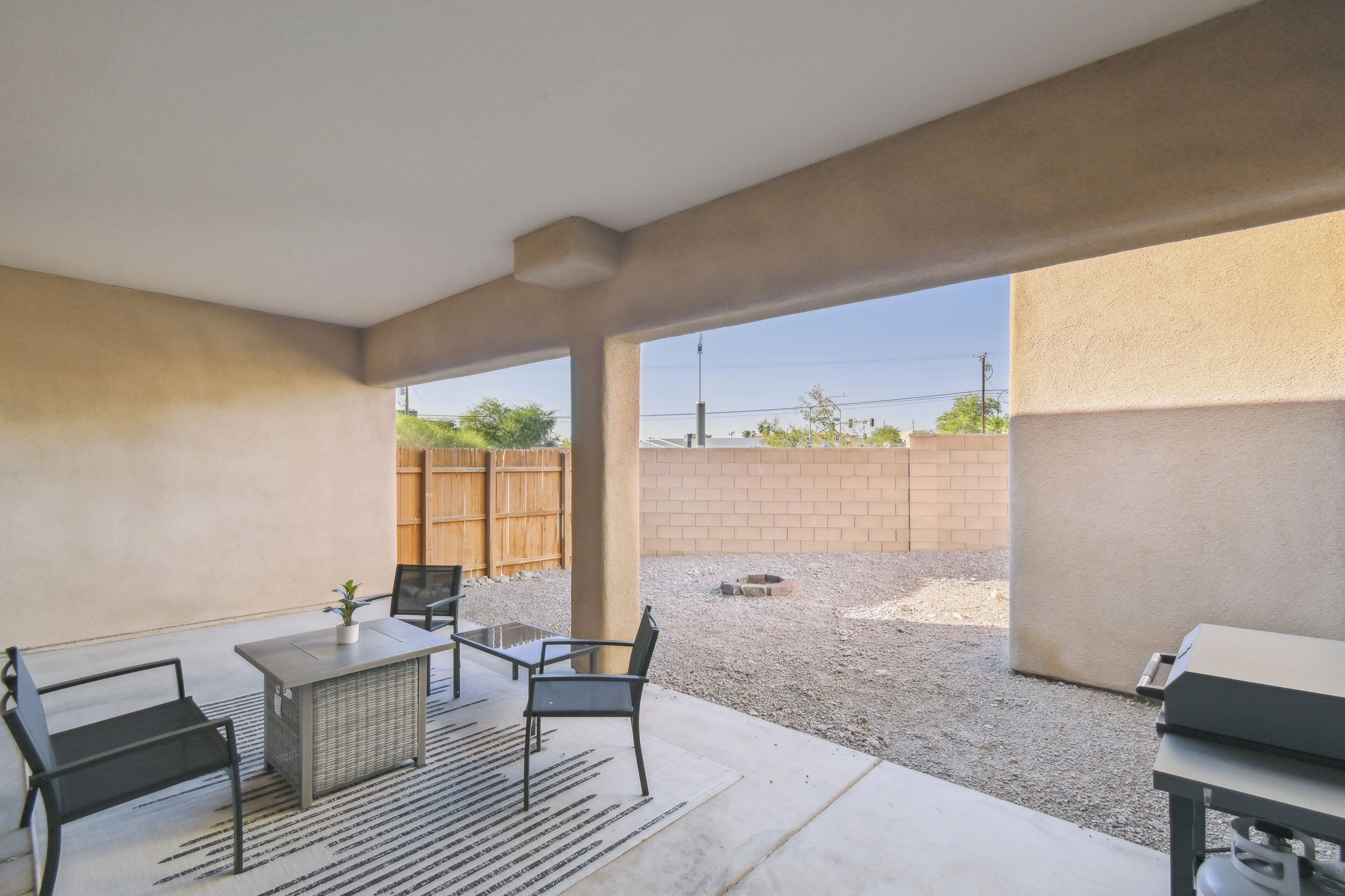 An outdoor patio area with a table and chairs, a grill, and a view of a brick wall and fence.