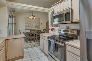 A modern kitchen with stainless steel appliances, wooden cabinets, and a dining area with a painting on the wall. - Lake Havasu Home Near Rotary Park + London Bridge! (Lake Havasu City)