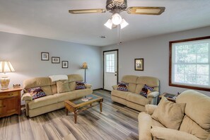 A living room with two beige sofas, a wooden coffee table, a ceiling fan, and a large window. - Wooded Cabin w/ Pool Table Near Dtwn Gatlinburg! (Gatlinburg)