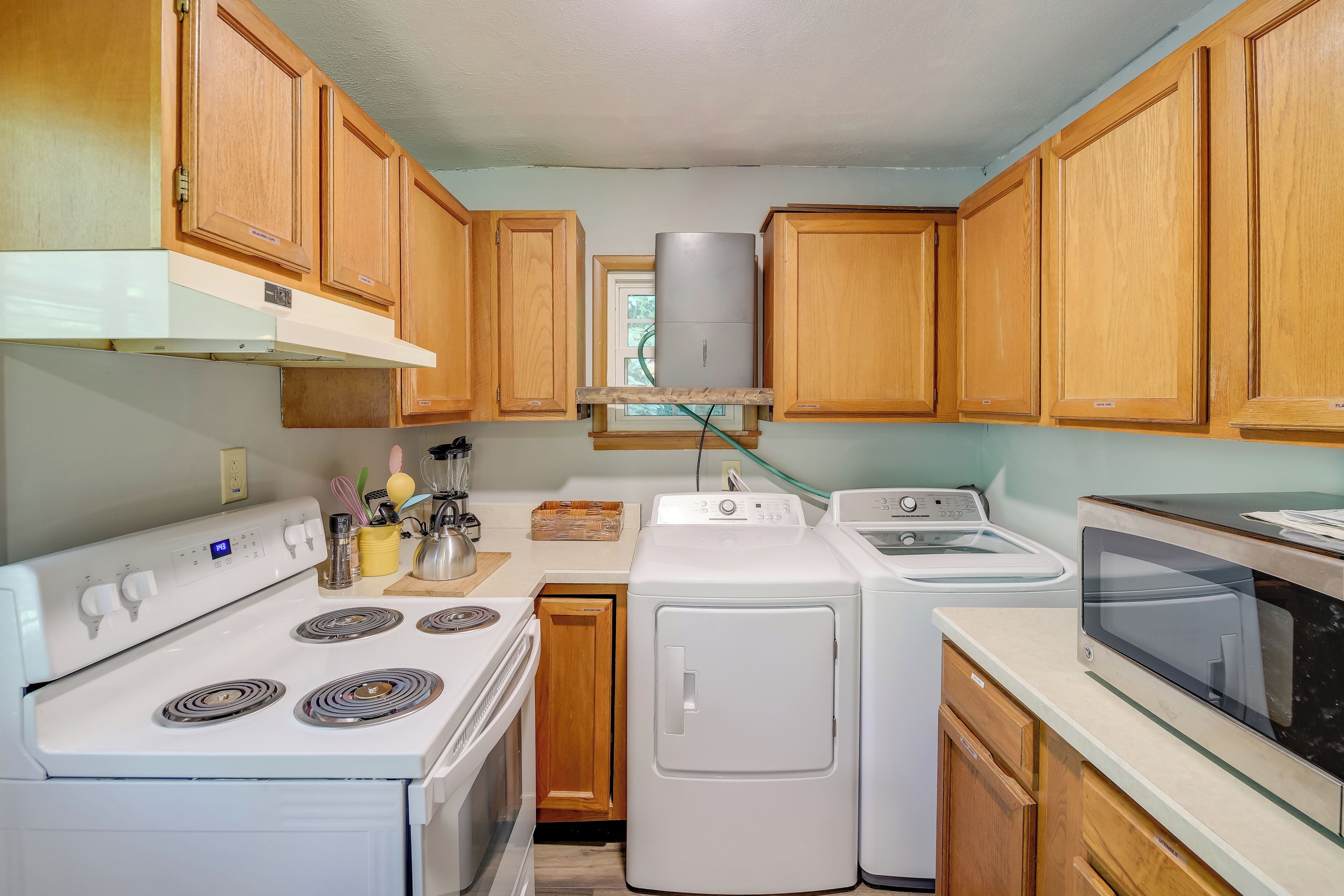 A kitchen with wooden cabinets, a white stove, a washing machine, a dryer, and a microwave.