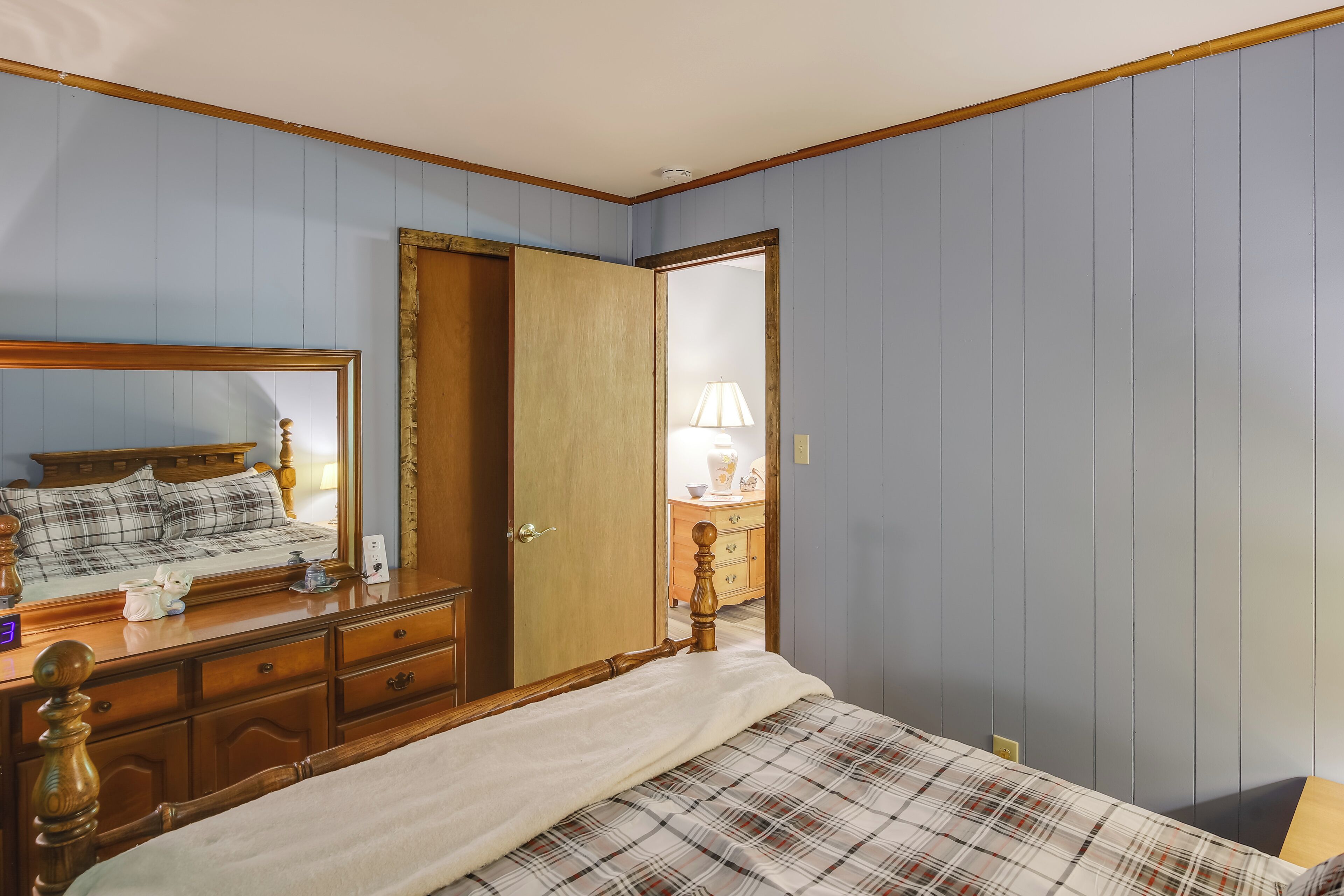 Une chambre à coucher comprenant un lit, une commode, un miroir et une porte donnant sur une autre pièce.