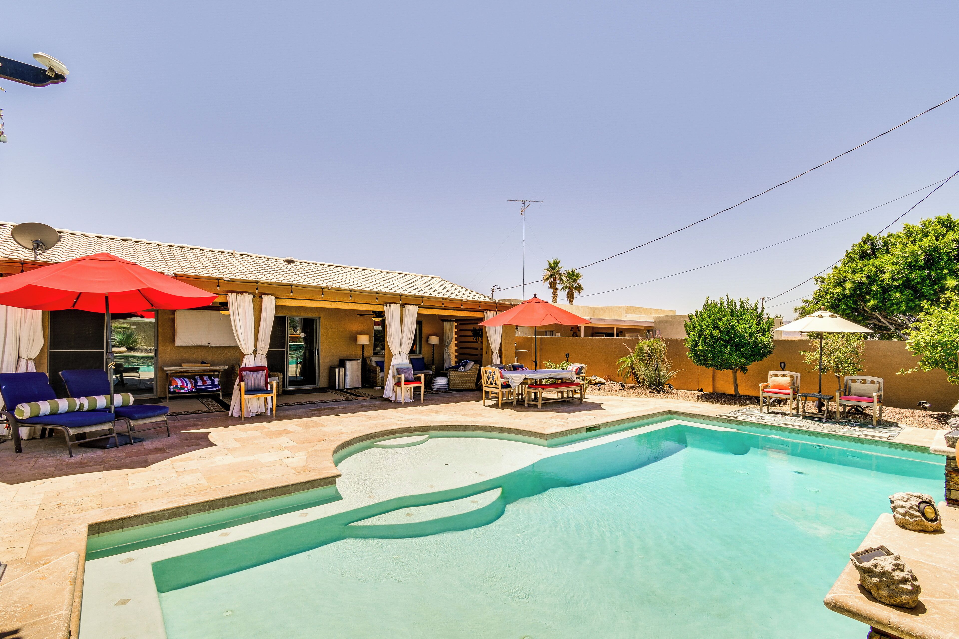 A pool area with lounge chairs and umbrellas, a covered seating area, and a building with a tiled roof.