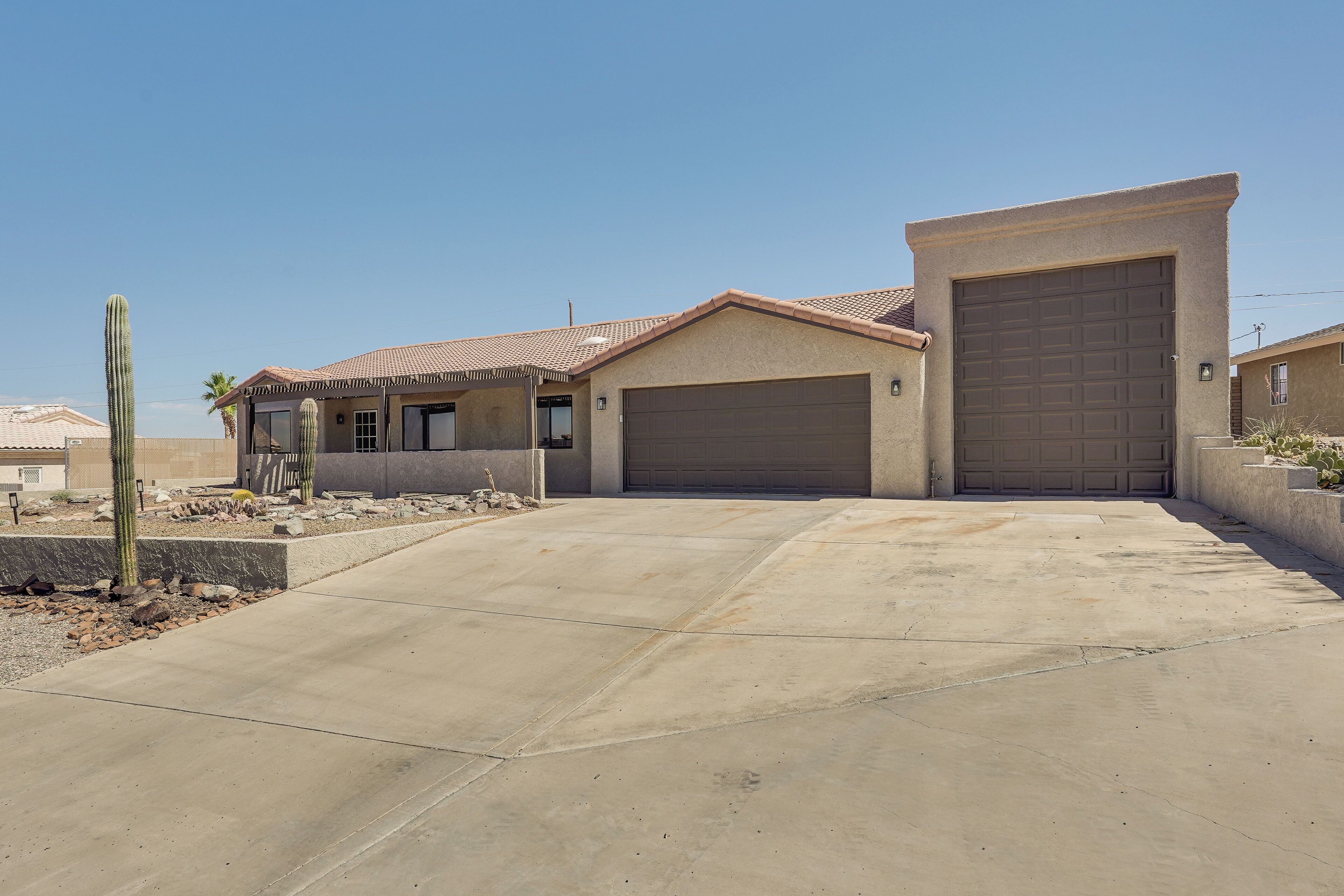 A residential house with a garage, a paved driveway, and a cactus in the garden.