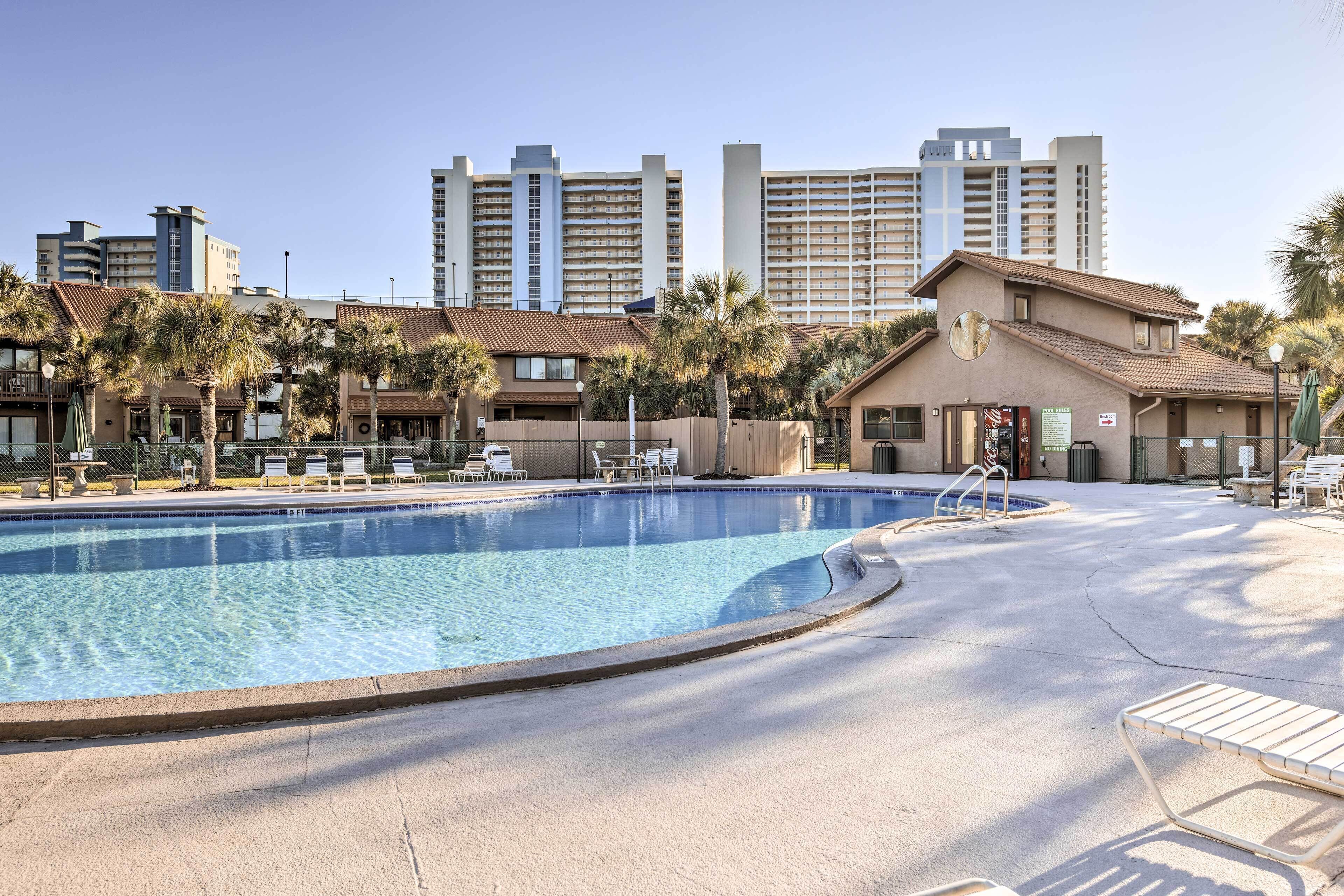 Ein Hotelpoolbereich mit klarem, blauem Wasser, Liegestühlen und Palmen.