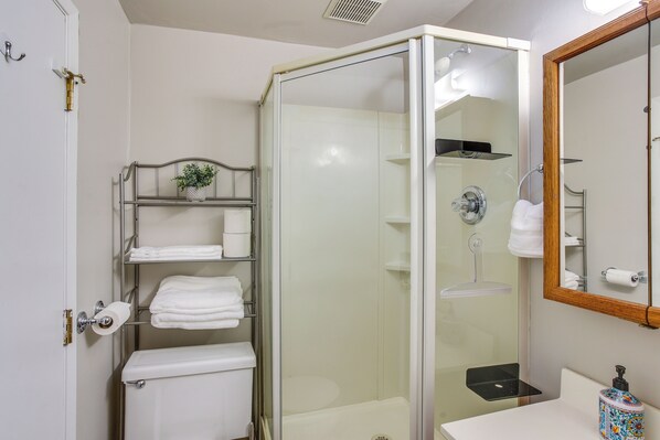Une salle de bain moderne avec une douche à parois de verre, des toilettes, un lavabo avec un miroir et des étagères avec des serviettes.