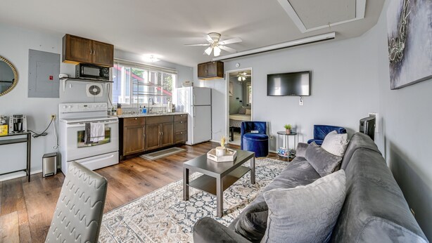 A modern kitchen with white appliances, a dining area with a gray sofa and patterned rug, and a ceiling fan. - Washington Vacation Rental Near Seattle & Tacoma (Des Moines)
