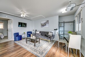 A modern living room with a grey sofa, a coffee table, and a blue chair. There is a television mounted on the wall, a ceiling fan, and a projector. - Washington Vacation Rental Near Seattle & Tacoma (Des Moines)