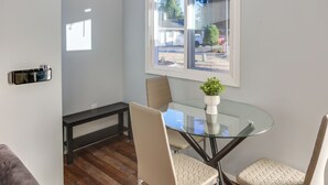 A modern dining area with a glass table, cushioned chairs, a bench, and a window with a view of the outside. - Washington Vacation Rental Near Seattle & Tacoma (Des Moines)