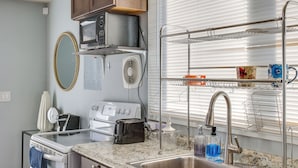A compact kitchen with a built-in oven, microwave, and toaster. It includes a stainless steel sink and a window with blinds. - Washington Vacation Rental Near Seattle & Tacoma (Des Moines)