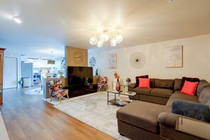 Ein modernes Wohnzimmer mit Sofa, Sessel und Couchtisch. Ein Fernseher, eine Uhr und Wanddekoration sind ebenfalls vorhanden.