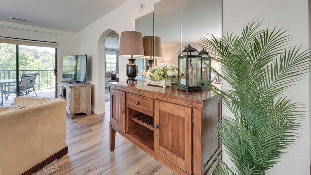 Una sala moderna con un mueble de madera, un sofá, un ventanal grande y una planta en maceta.