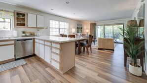 Una cocina moderna con una isla central, suelo de madera y un área de comedor con vistas al exterior.