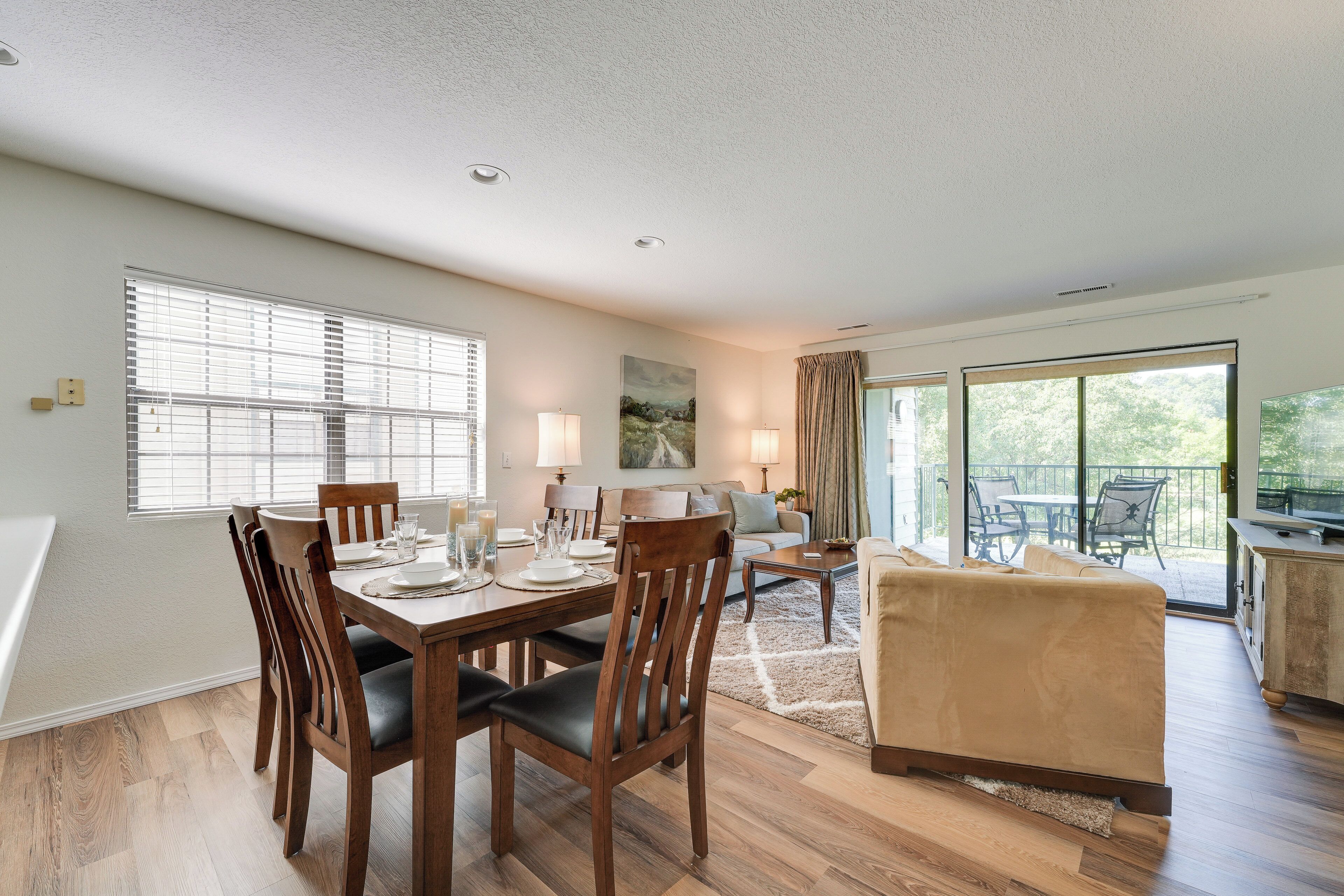 A spacious living area with a dining table set for four, a sofa, and a balcony with outdoor seating.