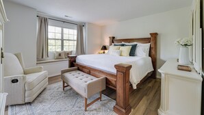 Un dormitorio con una cama grande, un banco, una silla y una mesita de noche.