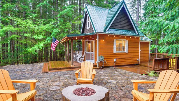 A cabin with a stone patio, wooden deck, and Adirondack chairs. - Adorable A-frame Cabin, Steps to Lake Cushman! (Hoodsport)